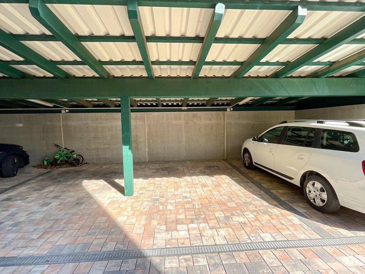 Überdachter Carport mit mehreren Stellplätzen für Fahrzeuge auf gepflastertem Boden.