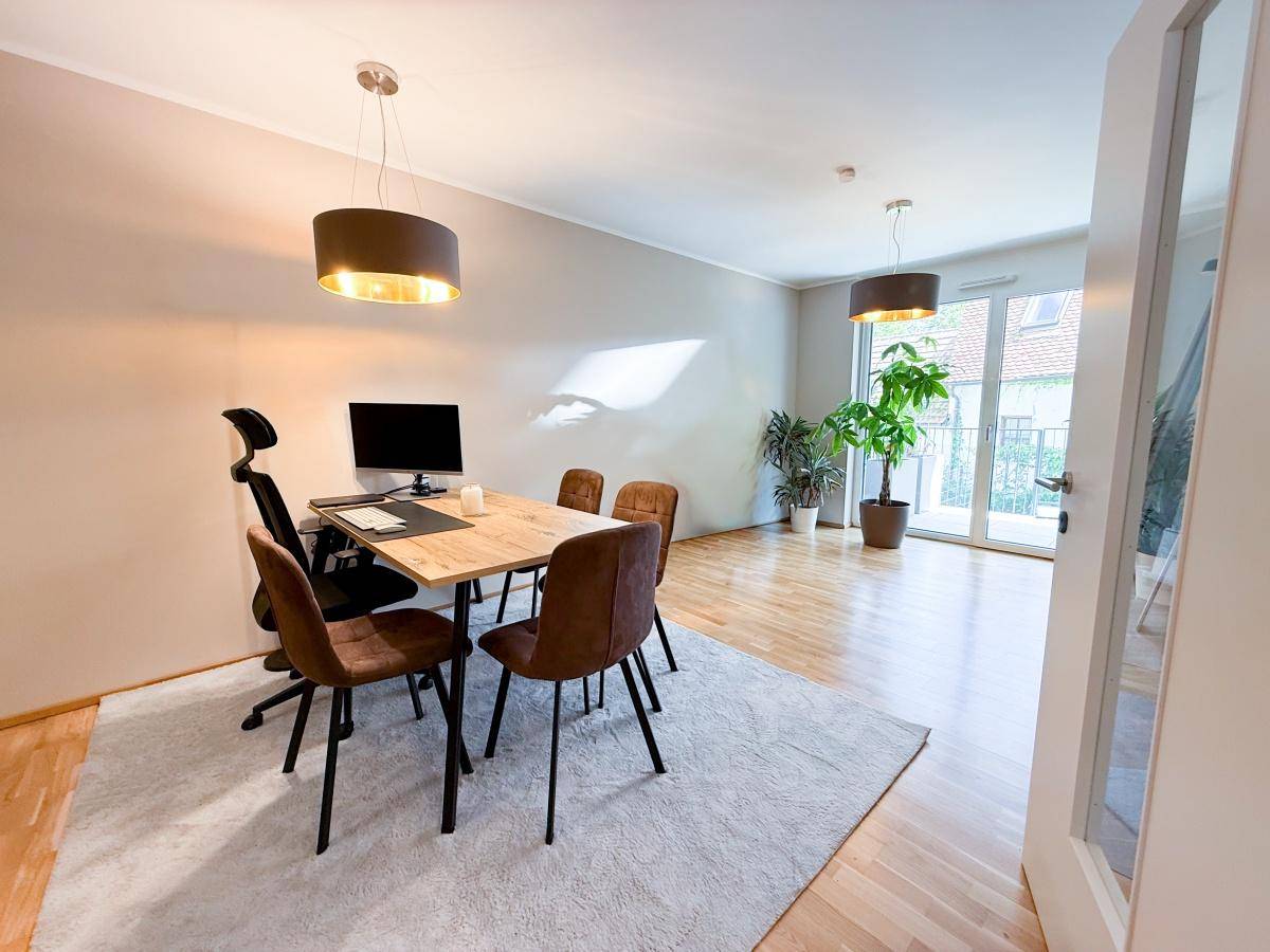 Offener Wohn- und Essbereich mit hellem Parkettboden, modernem Esstisch und Zugang zum Balkon.