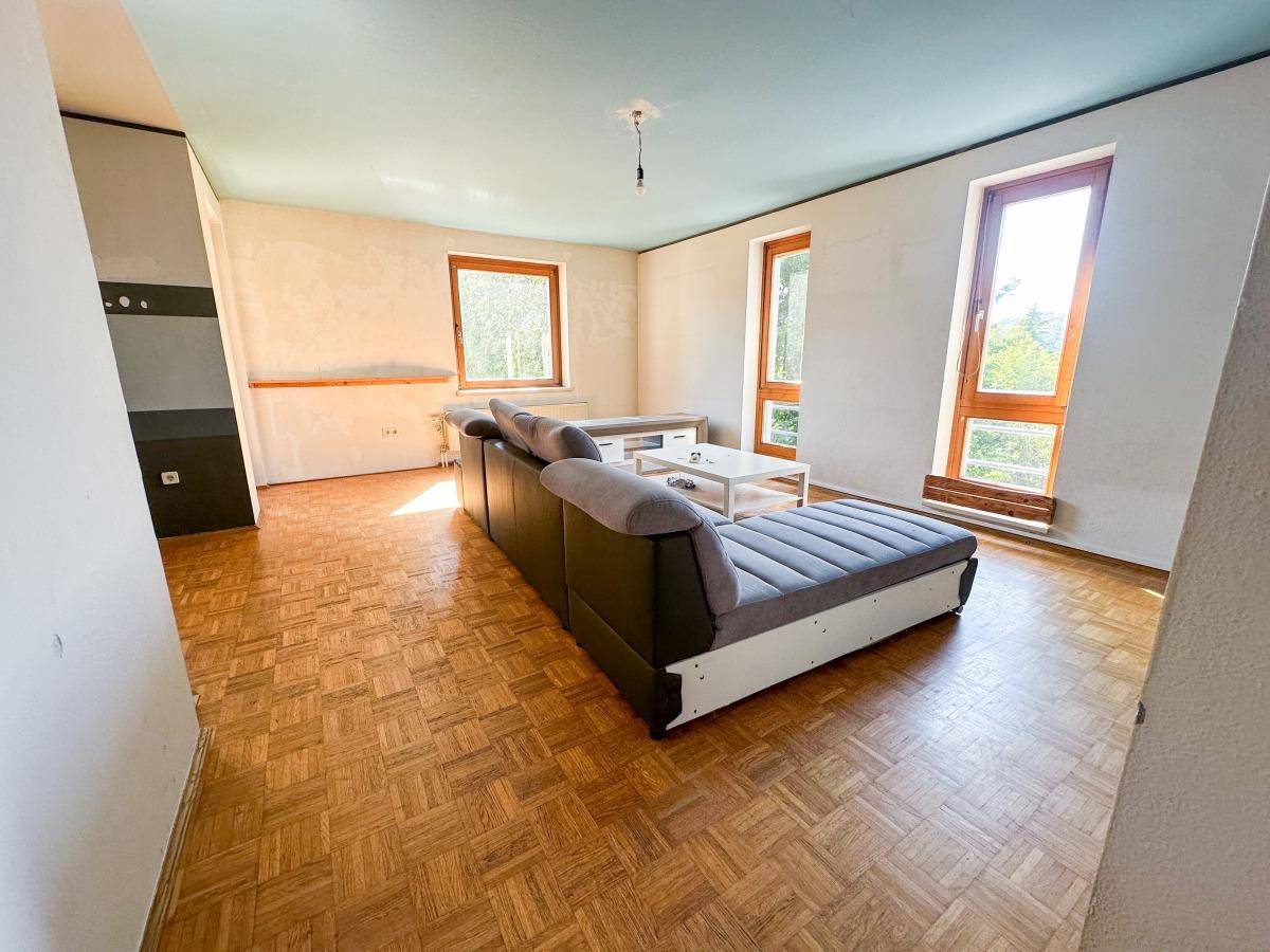 Geräumiges Wohnzimmer mit bequemer Couch, Parkettboden und großen Fenstern für viel Licht.