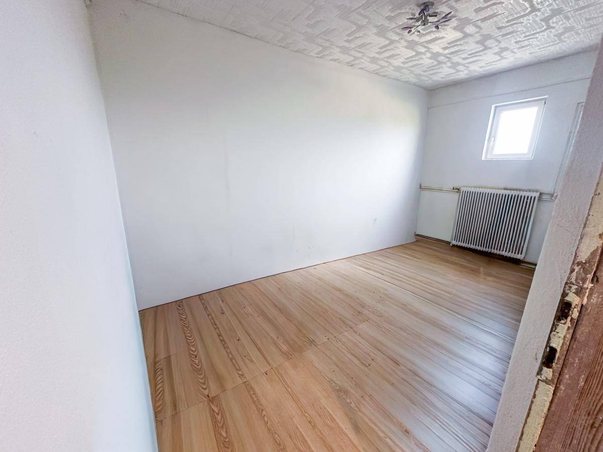 Helles Schlafzimmer mit Holzoptik-Boden und Fenster mit Rollladen.