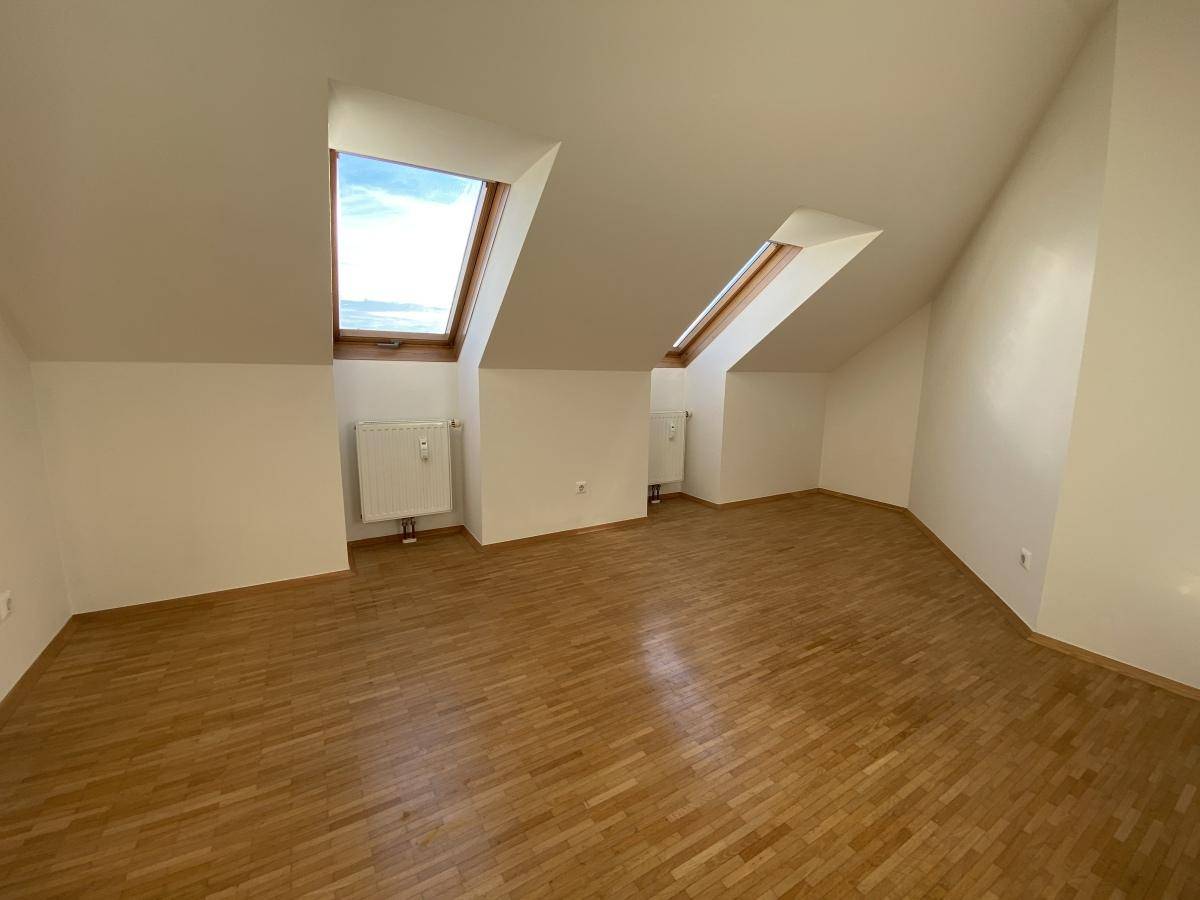 Geräumiges Dachgeschosszimmer mit Holzboden, schrägen Wänden und zwei Dachfenstern für Tageslicht.