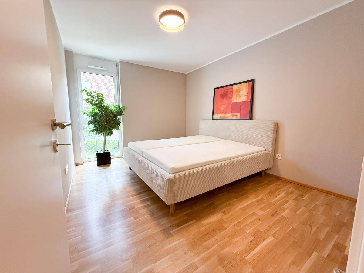 Gemütliches Schlafzimmer mit Doppelbett, hellem Parkettboden und Zugang zu einem Außenbereich.