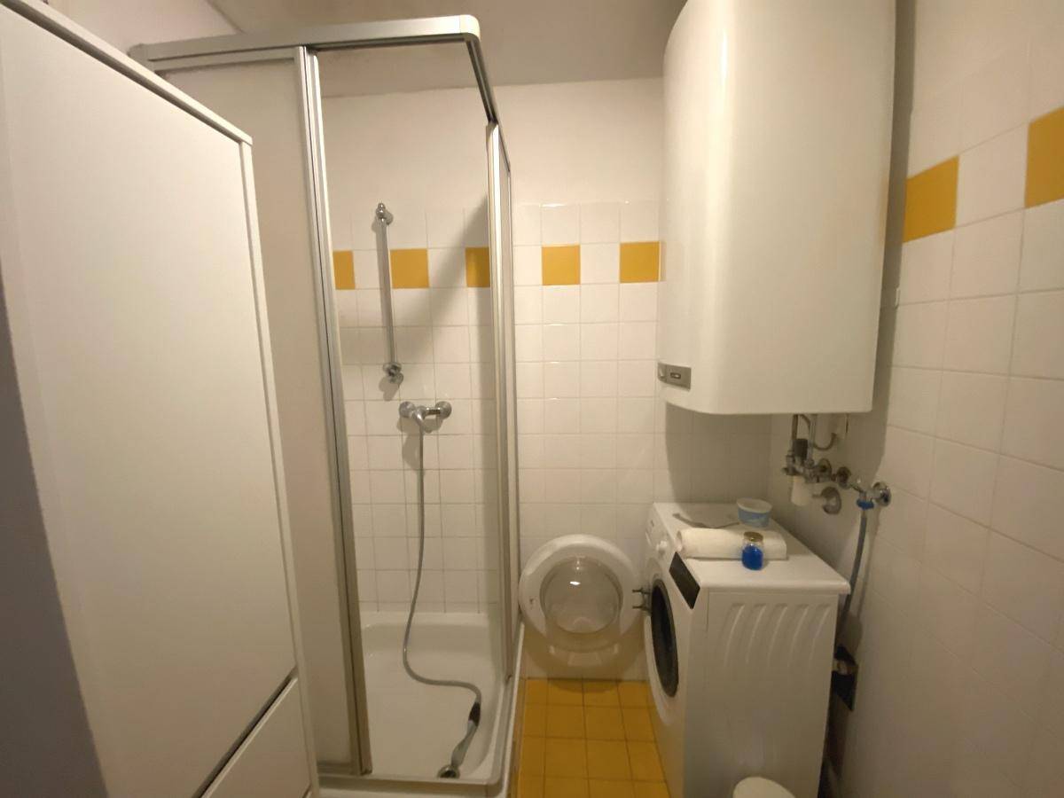 Badezimmer mit Duschkabine, Waschmaschine und gelben Akzentfliesen.