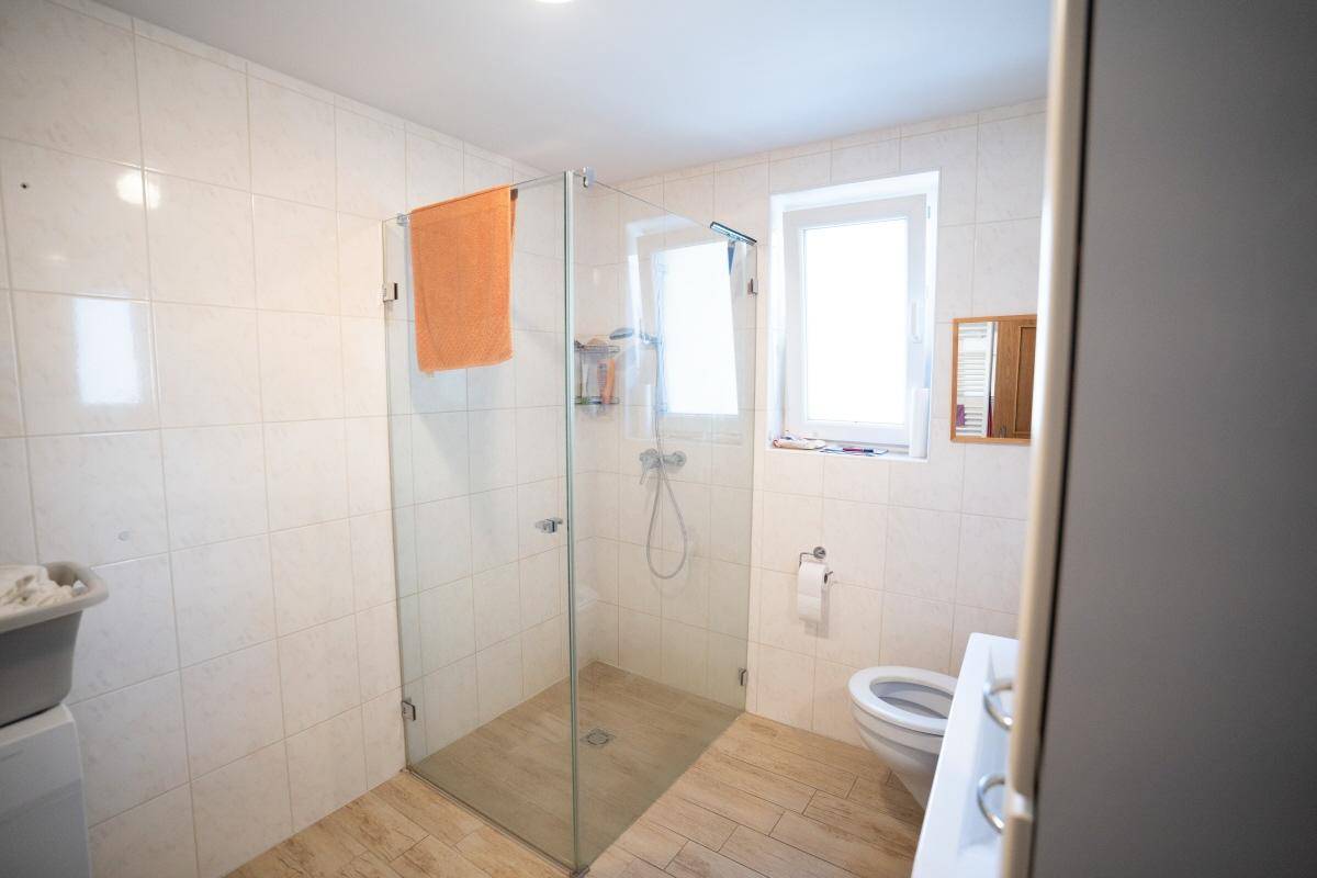 Modernes Badezimmer mit großer begehbarer Dusche, WC und Fenster.
