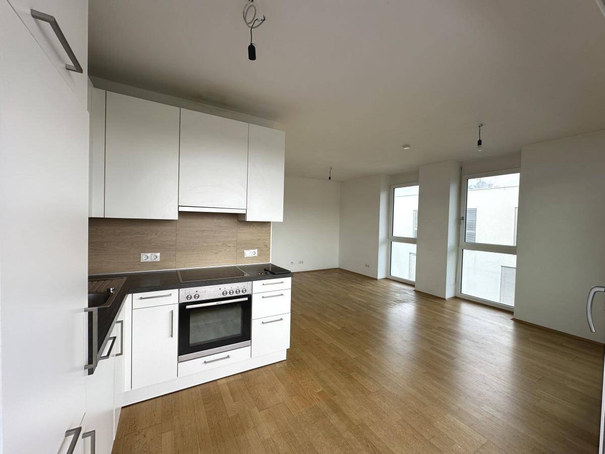 Funktionale Küchenzeile mit weißen Schränken und integriertem Backofen, offen zum Wohnbereich.