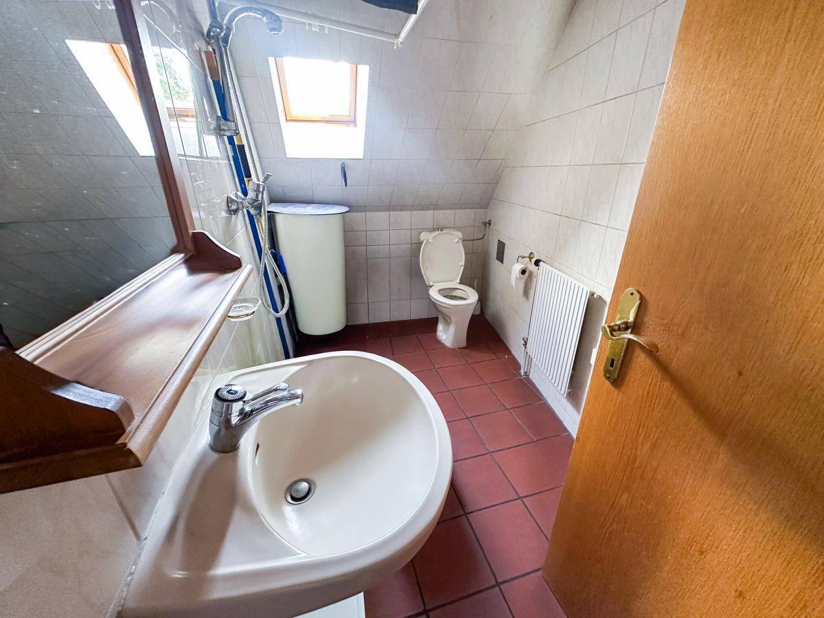 Badezimmer im Dachgeschoss mit Dusche, Waschbecken, Toilette, Dachfenster und Terrakottafliesen.