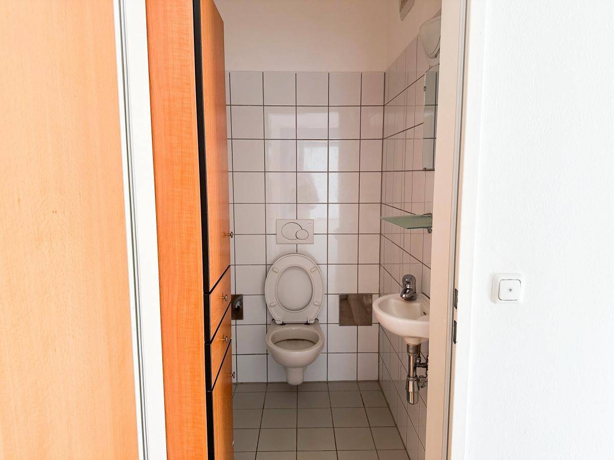 Kleines Gäste-WC mit weißen Fliesen, Toilette und Handwaschbecken.