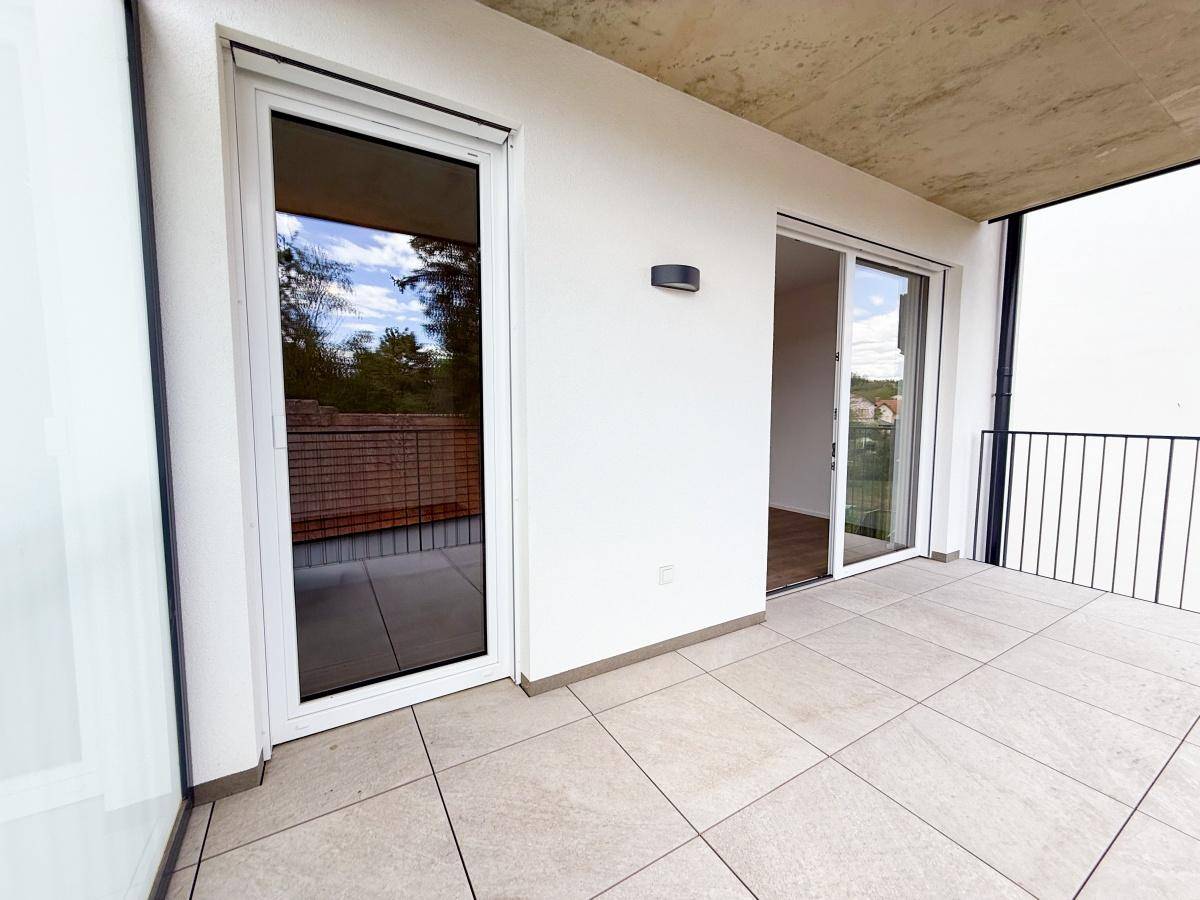 Heller Balkon mit Fliesenboden und Zugang zu den Innenräumen durch große Fenster.