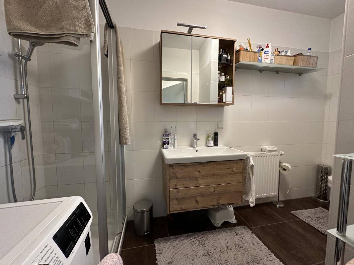 Badezimmer mit Duschkabine, Waschbeckenunterschrank und Spiegelschrank, hell gefliest und gut ausgestattet.