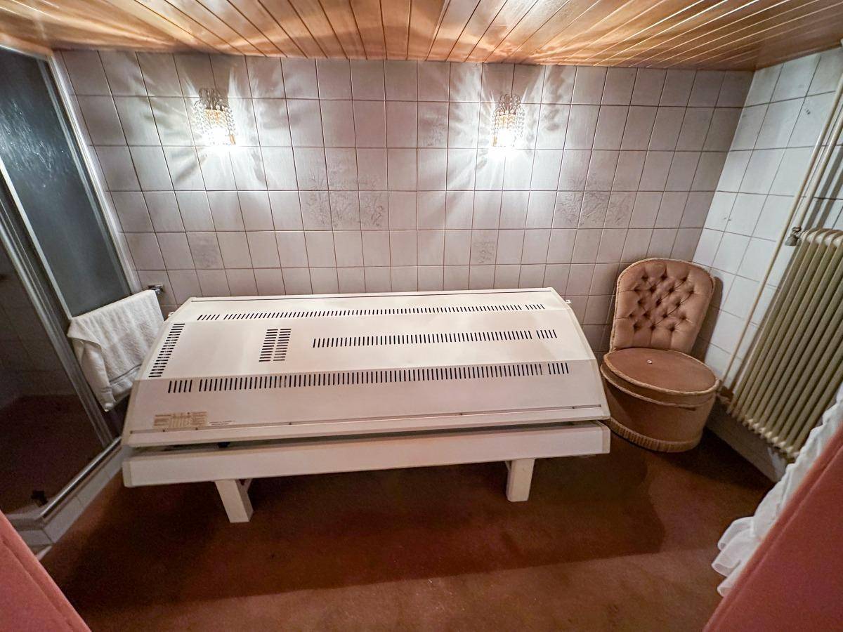 Wellnessbereich mit Solarium, Duschkabine und gefliesten Wänden.