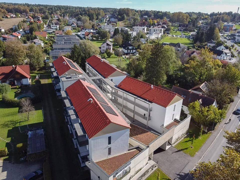 Luftaufnahme eines Wohnkomplexes mit Photovoltaikanlagen und umliegender grüner Landschaft.