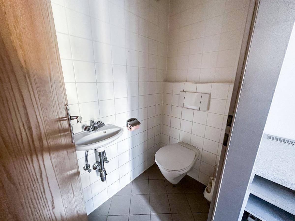 Kleines Gäste-WC mit weißen Fliesen, wandmontierter Toilette und Waschbecken.