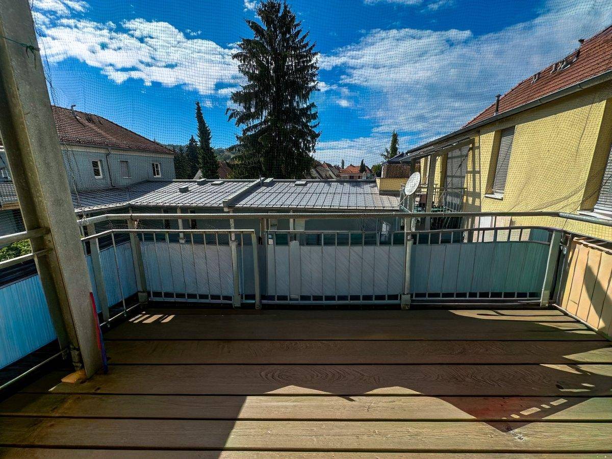 Balkon mit Holzboden und Blick auf die umliegenden Gebäude und Bäume.
