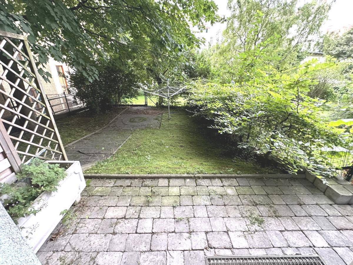 Gepflasterte Terrasse mit Zugang zu einem grünen Gartenbereich und Wäscheleine.