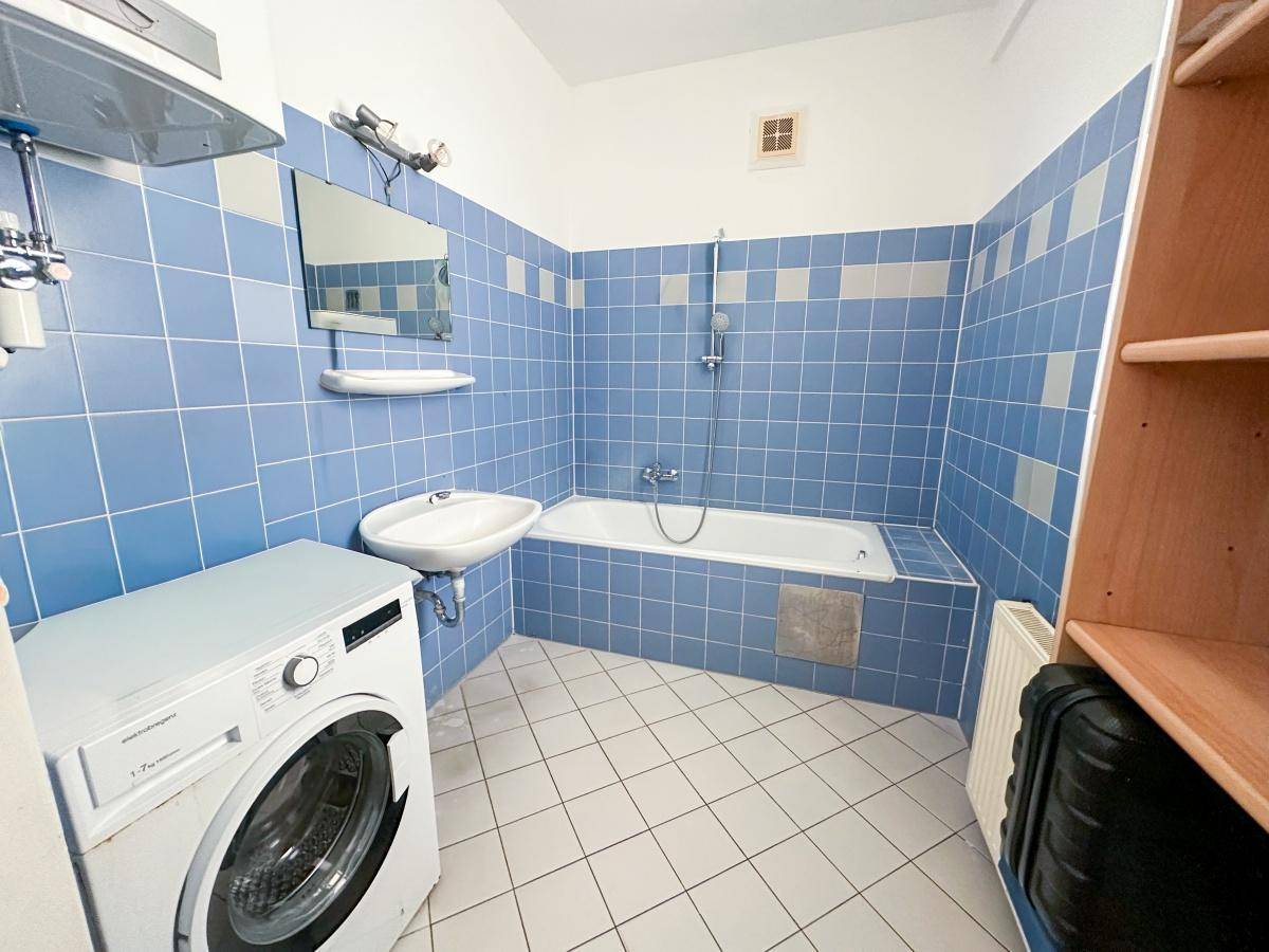 Badezimmer mit blauen Fliesen, Badewanne, Waschbecken und einer Waschmaschine.
