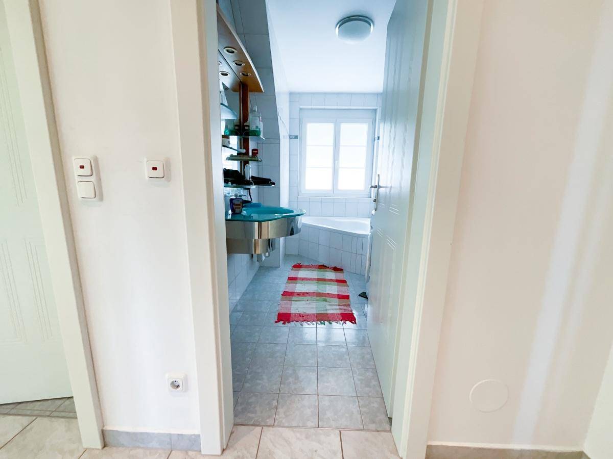 Flur mit Fliesenboden und Blick in ein Badezimmer mit Eckbadewanne.