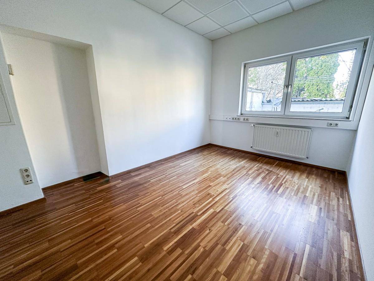 Geräumiges Büro mit viel Tageslicht durch große Fenster und warmem Holzboden.