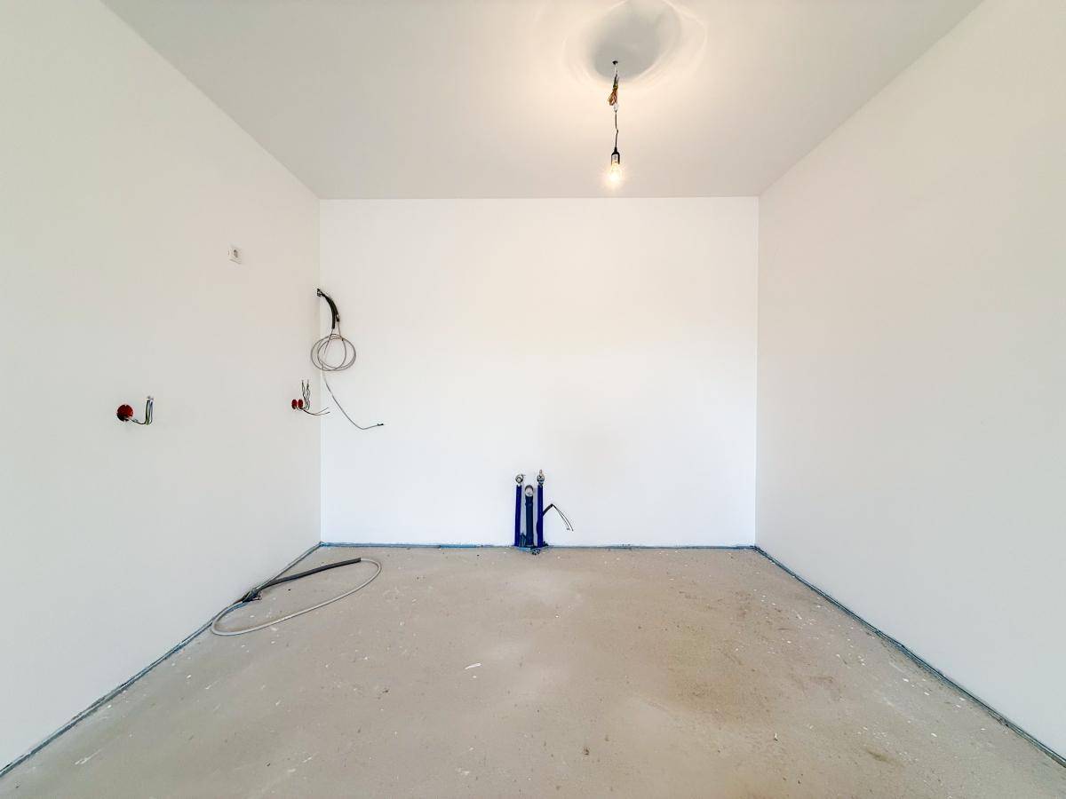 Rohbau einer Küche mit sichtbaren Wasseranschlüssen und blankem Estrichboden für die Installation.
