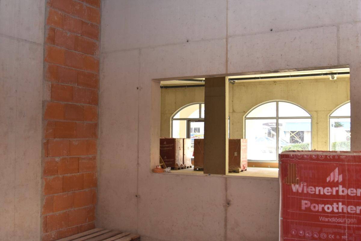 Rohbau mit Betonwänden, einem Durchbruch und gestapelten Ziegeln, mit Blick auf Bogenfenster.