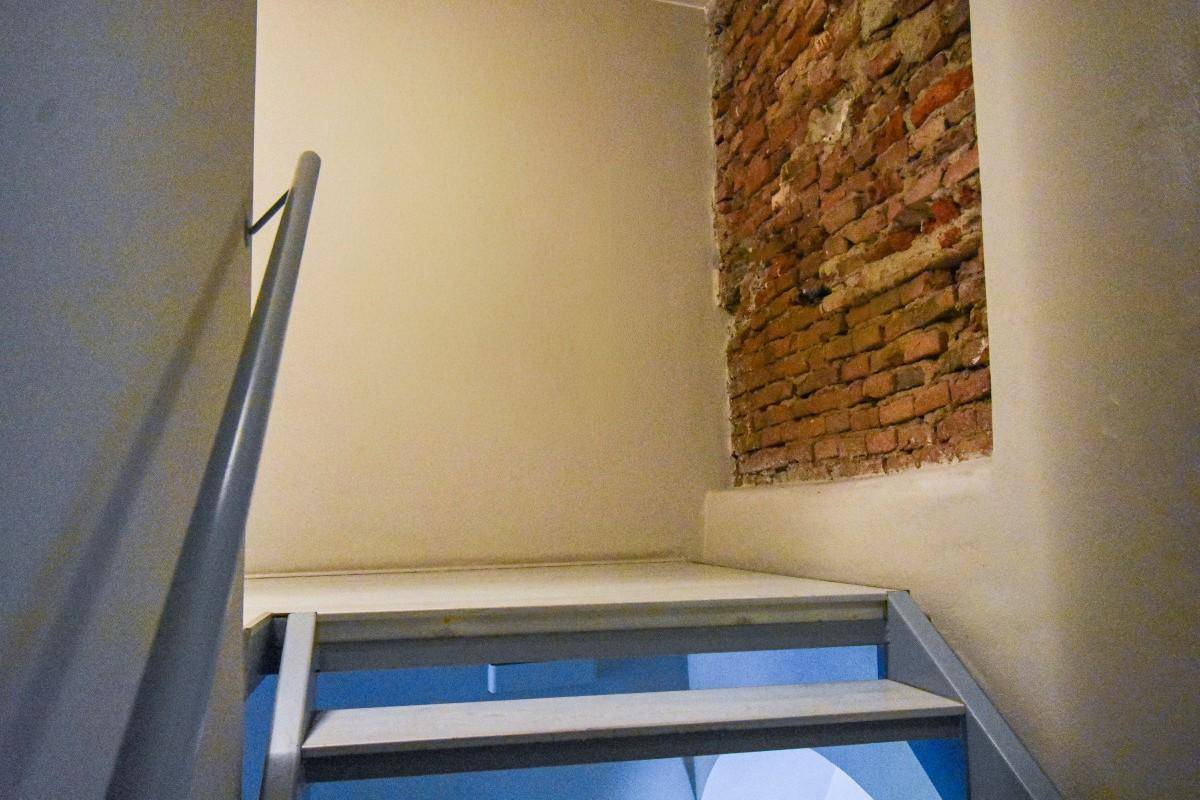 Treppenabsatz mit freigelegter Ziegelwand und schlichtem Geländer, das zu weiteren Ebenen führt.