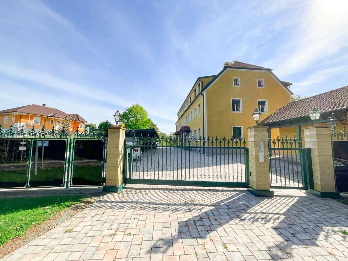 Zufahrt zu einem Wohngebäude mit großem Eingangstor und gepflastertem Vorplatz.