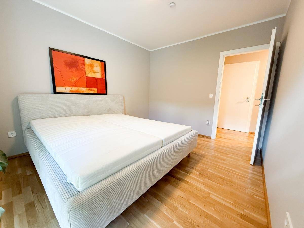 Schlafzimmer mit Doppelbett, modernem Bild und Parkettboden.