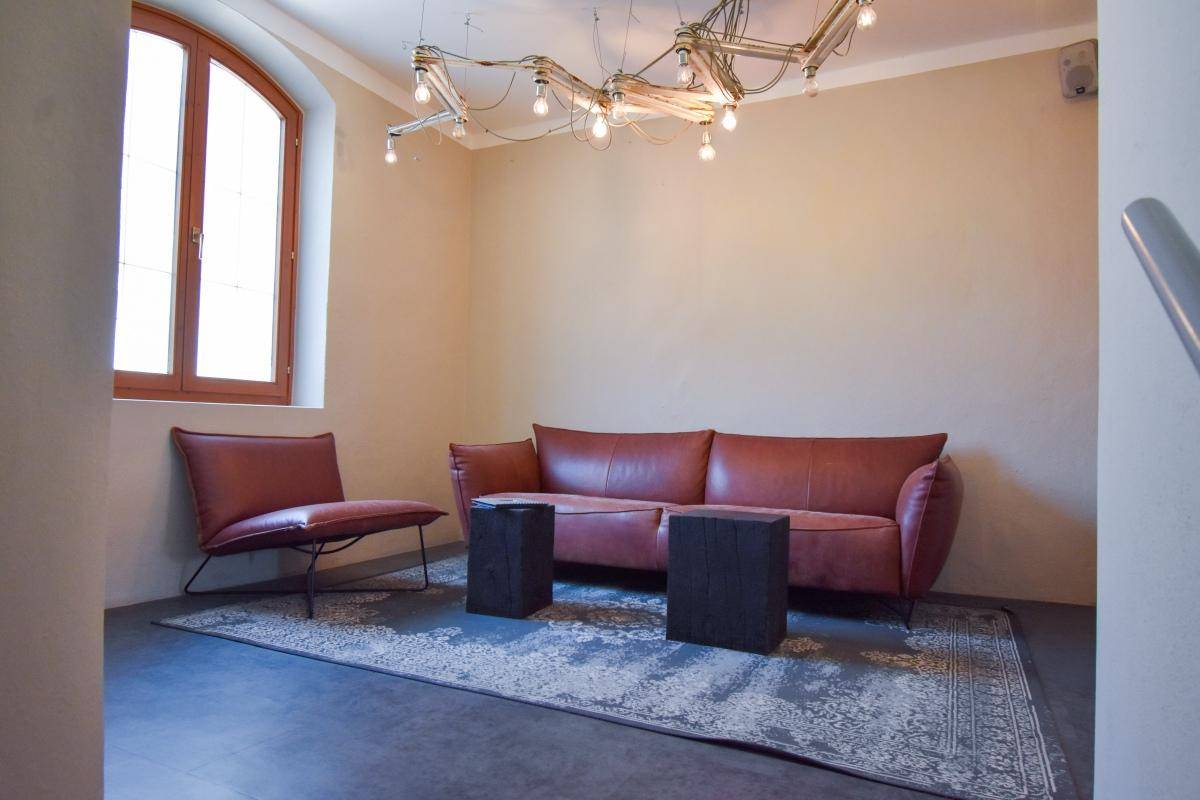 Gemütliches Wohnzimmer mit rotem Ledersofa, passendem Sessel und einem großen Rundbogenfenster.