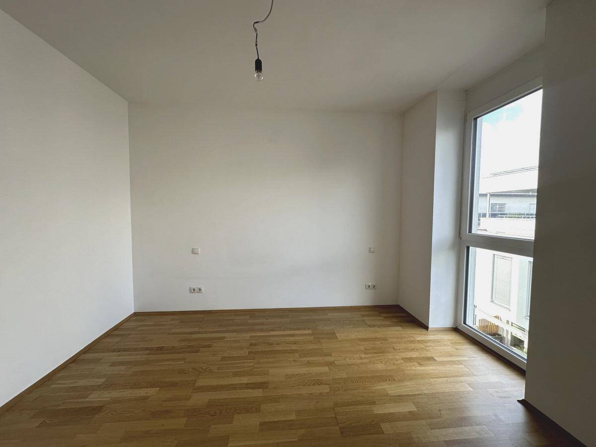 Helles Schlafzimmer mit Parkettboden und einem hohen Fenster, bereit zur individuellen Gestaltung.