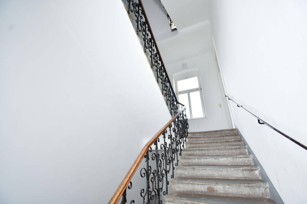 Helles Treppenhaus mit Steinstufen, schmiedeeisernem Geländer und Fenster.