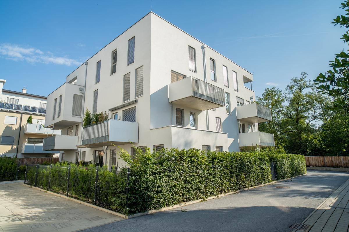 Zeitgenössisches Wohngebäude mit klarer Architektur, Balkonen und einer grünen Hecke im Vordergrund.