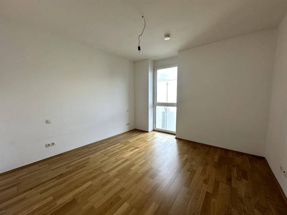 Geräumiges Schlafzimmer mit hellem Parkettboden und einem Fenster, das viel Tageslicht hereinlässt.
