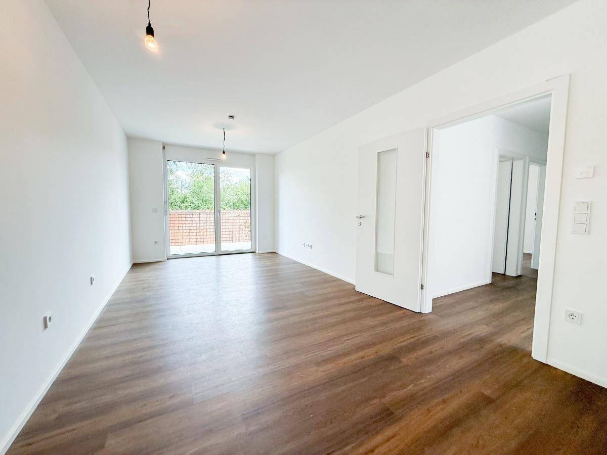 Heller Wohnbereich mit großen Fenstern, Laminatboden und Zugang zum Balkon.