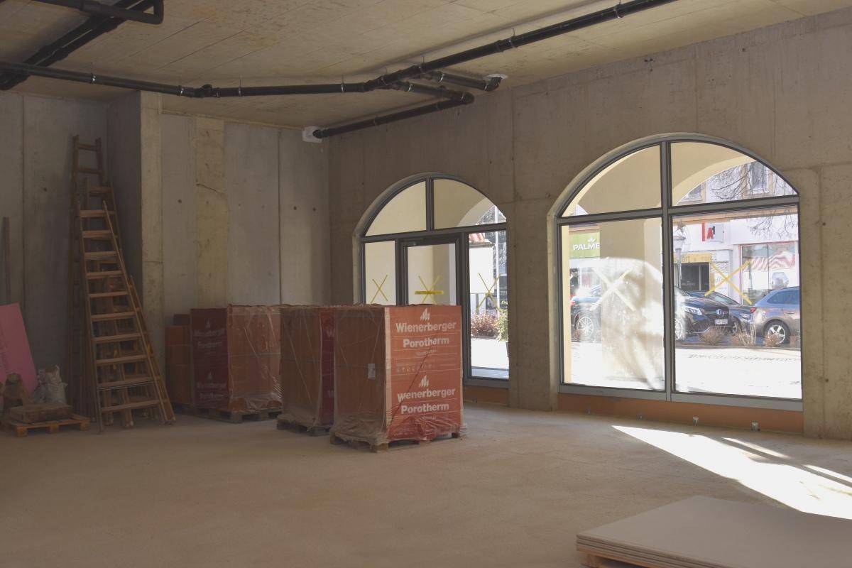 Rohbau eines Gewerberaums mit unverputzten Betonwänden, sichtbaren Leitungen und großen Bogenfenstern.