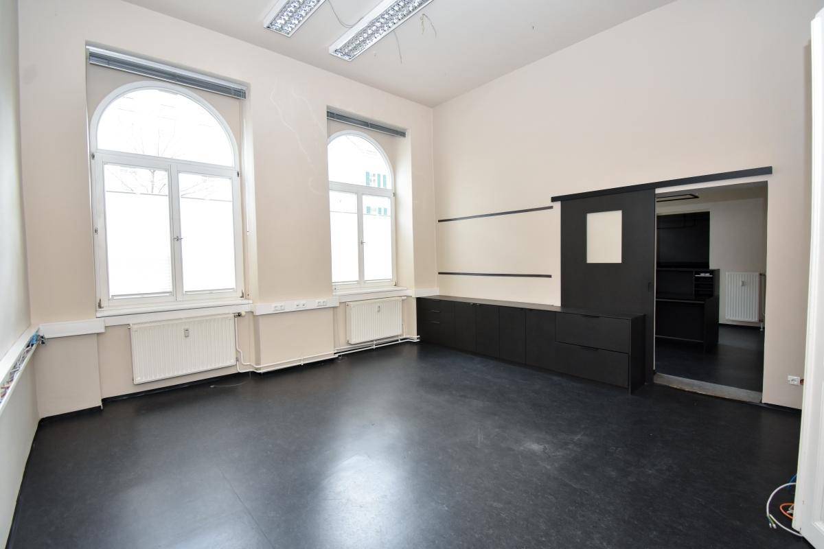 Geräumiger Büroraum mit hohen Decken, großen Bogenfenstern und dunklem Vinylboden, bereit zur Einrichtung.