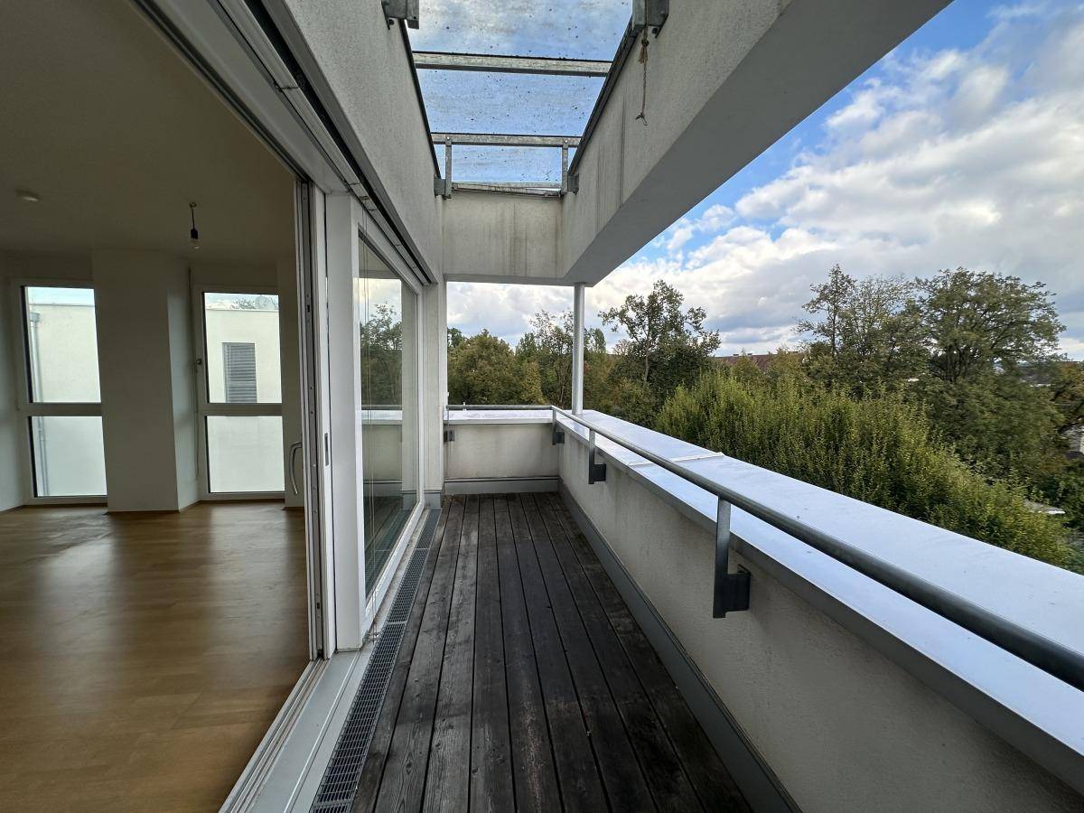 Geräumiger Balkon mit Holzboden und weitem Blick ins Grüne unter einem bewölkten Himmel.