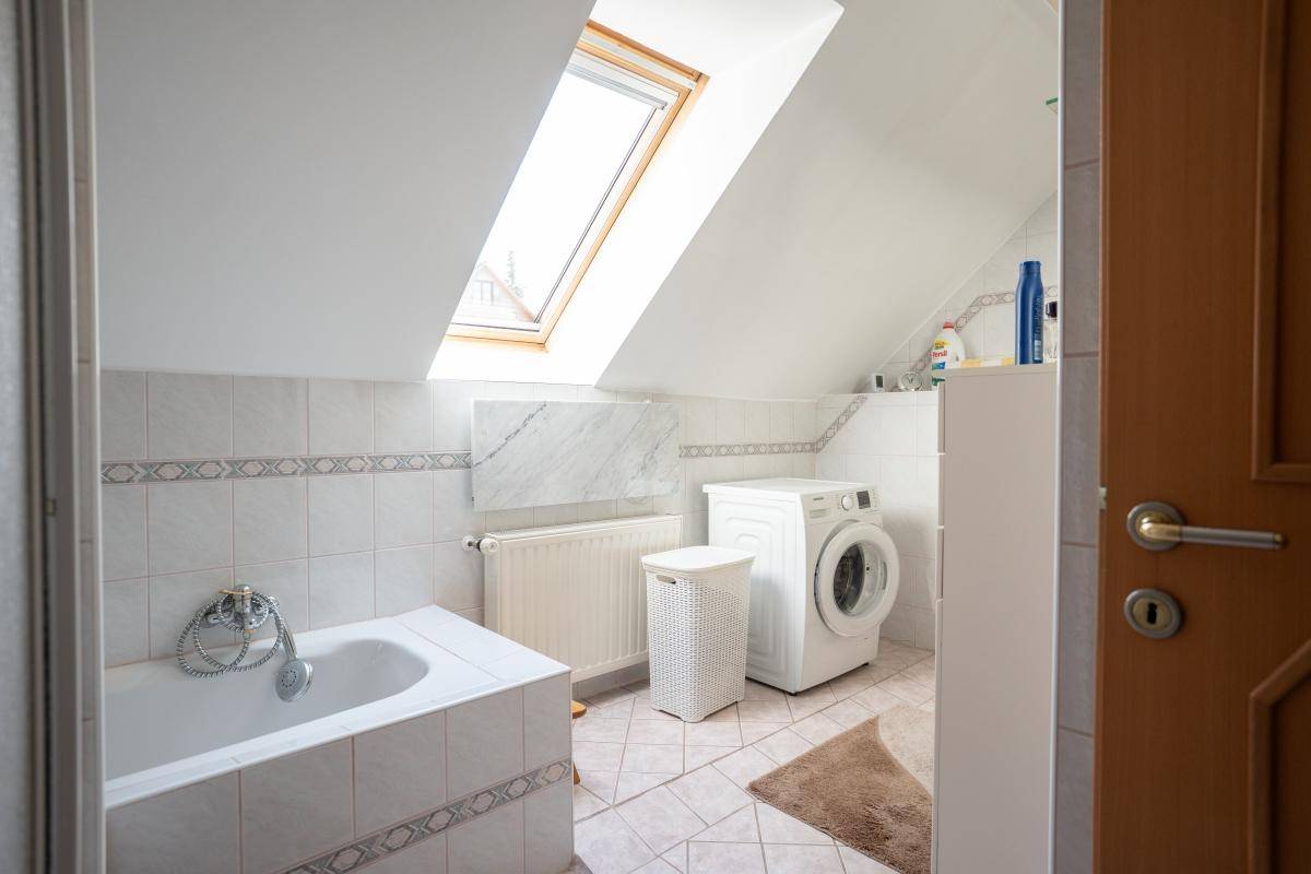 Helles Badezimmer im Dachgeschoss mit Badewanne, Waschmaschine und Dachfenster.