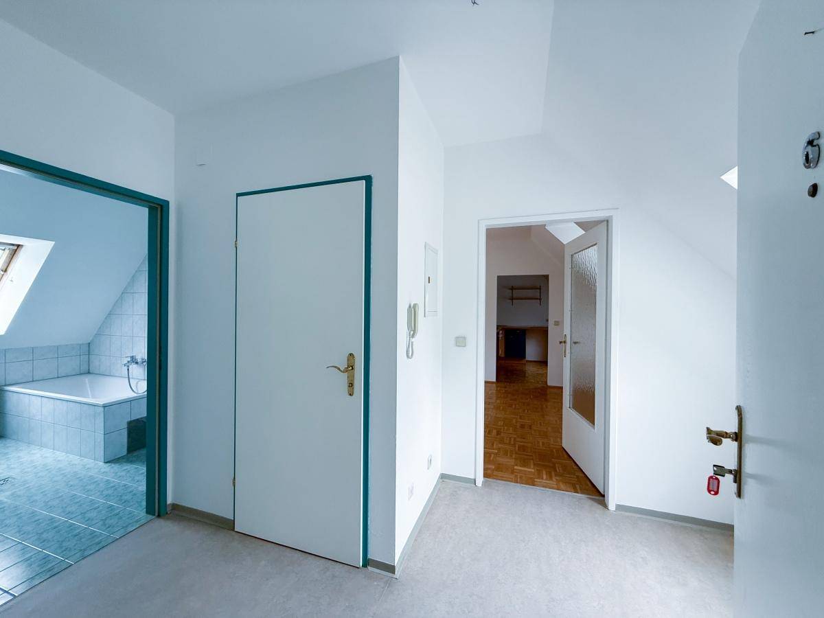 Flur mit hellem Bodenbelag und Zugang zu verschiedenen Räumen, inklusive dem Badezimmer.