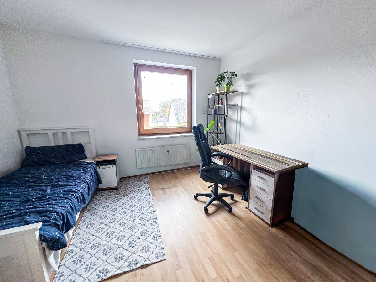 Kinderzimmer oder Arbeitszimmer mit Einzelbett, Schreibtisch und Laminatboden.