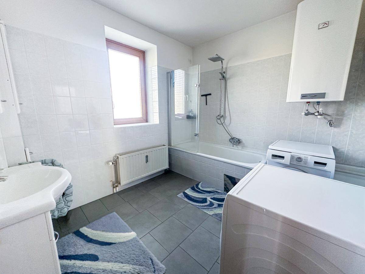Modernisiertes Badezimmer mit Dusche in der Badewanne, Waschmaschine und Fenster.
