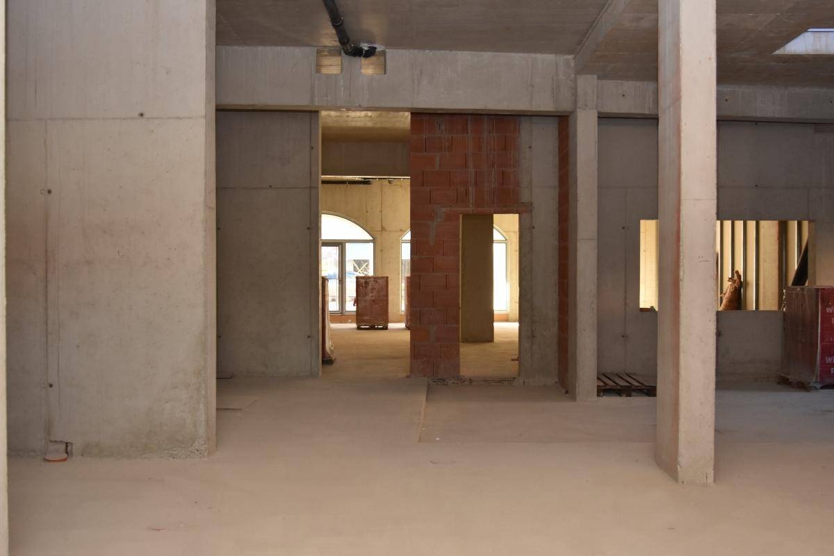 Rohbau mit Beton- und Ziegelwänden, Säulen und Blick in angrenzende Räume mit Bogenfenstern.