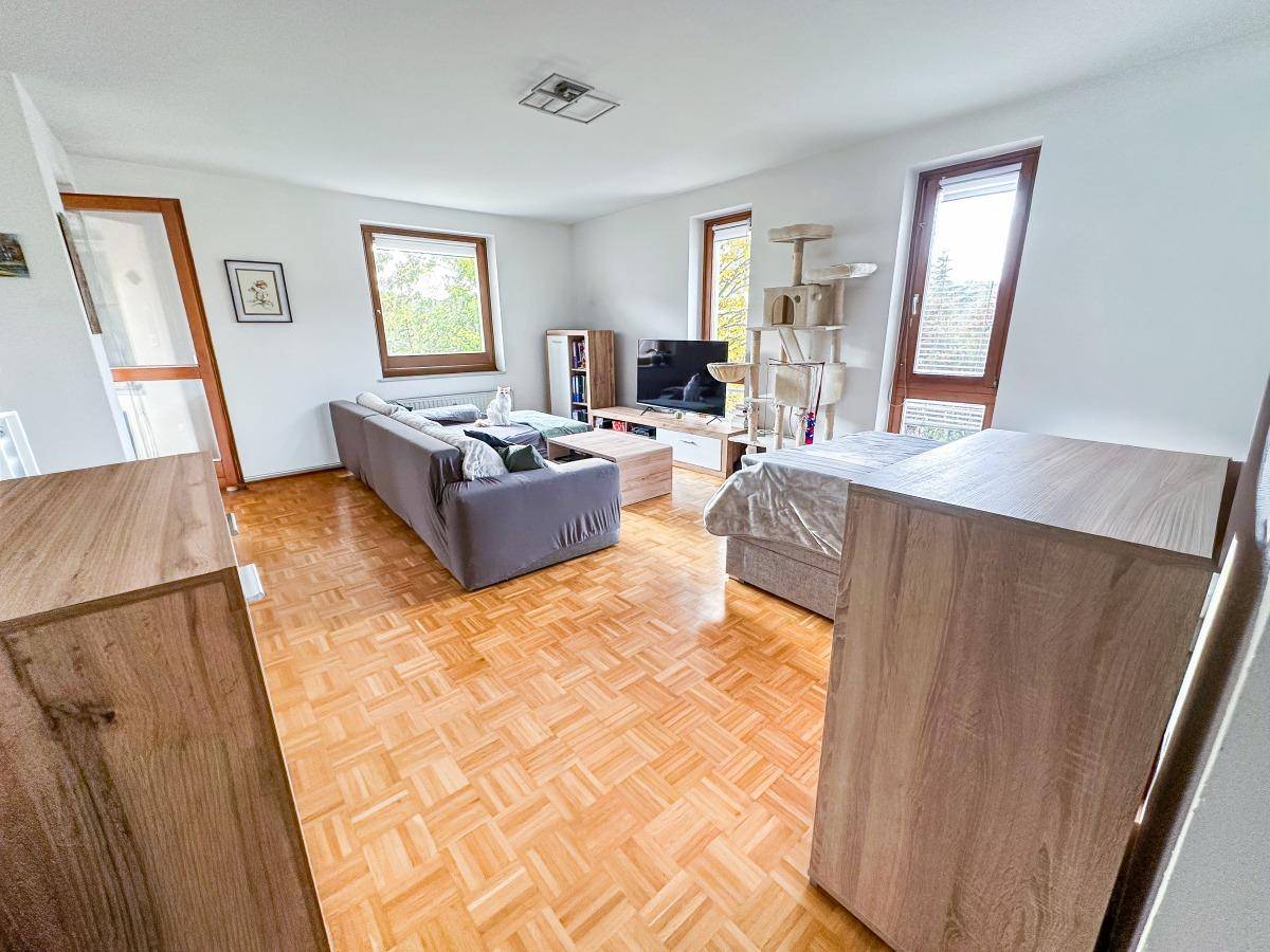 Geräumiges Wohnzimmer mit Parkettboden, bequemer Couch und Zugang zu einem Balkon.