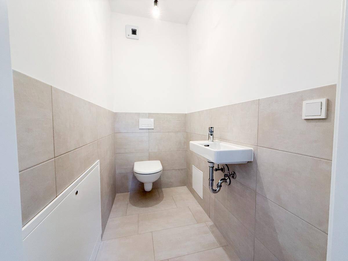 Separates Gäste-WC mit Wand-WC, Waschbecken und hellen Fliesen.