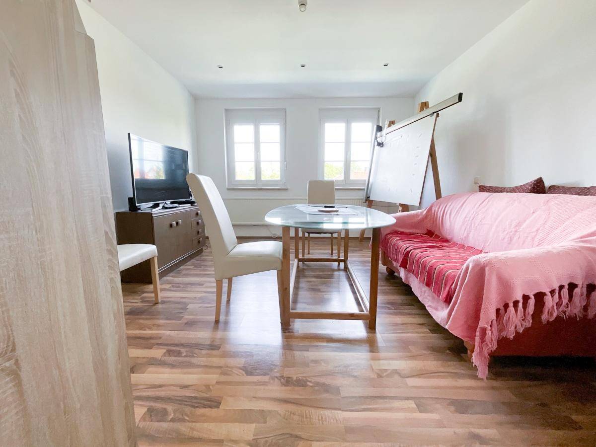 Heller Wohnraum mit Holzboden, Sofa und Fenstern, ideal als Büro nutzbar.
