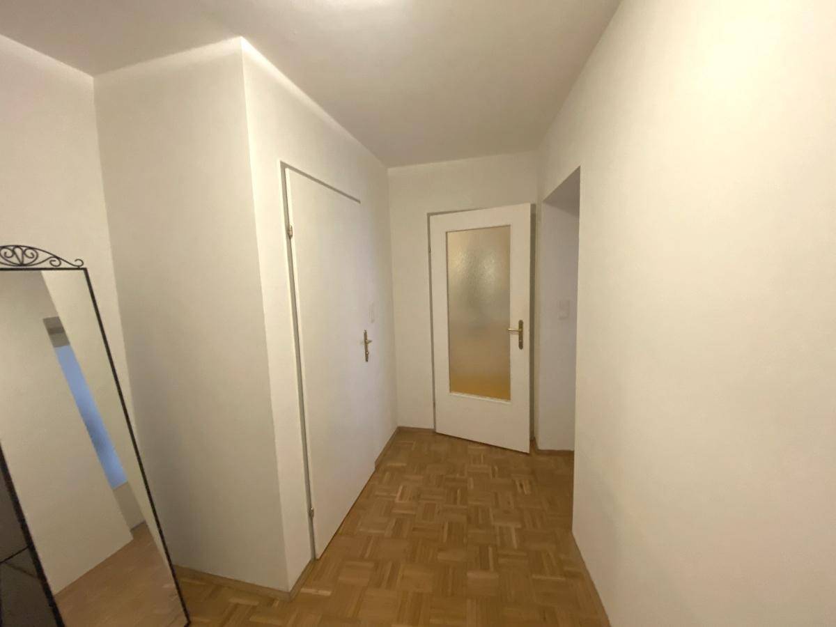 Heller Eingangsbereich mit Parkettboden und einem großen Spiegel.