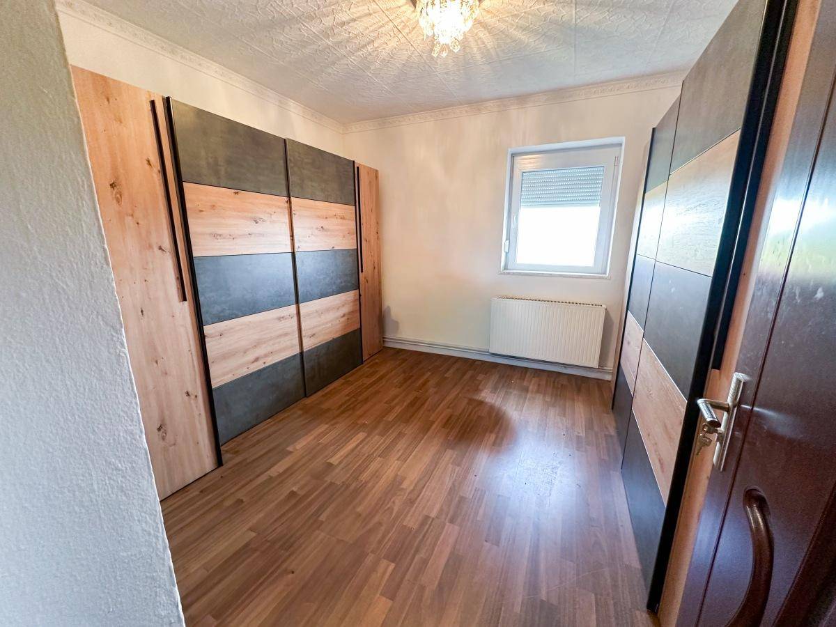 Schlafzimmer mit Einbauschränken, Holzoptik-Boden und Fenster mit Rollladen.