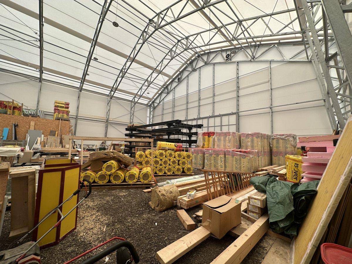 Geräumiger Innenraum der Lagerhalle mit hoher Decke, Stahlkonstruktion und gelagerten Baumaterialien.
