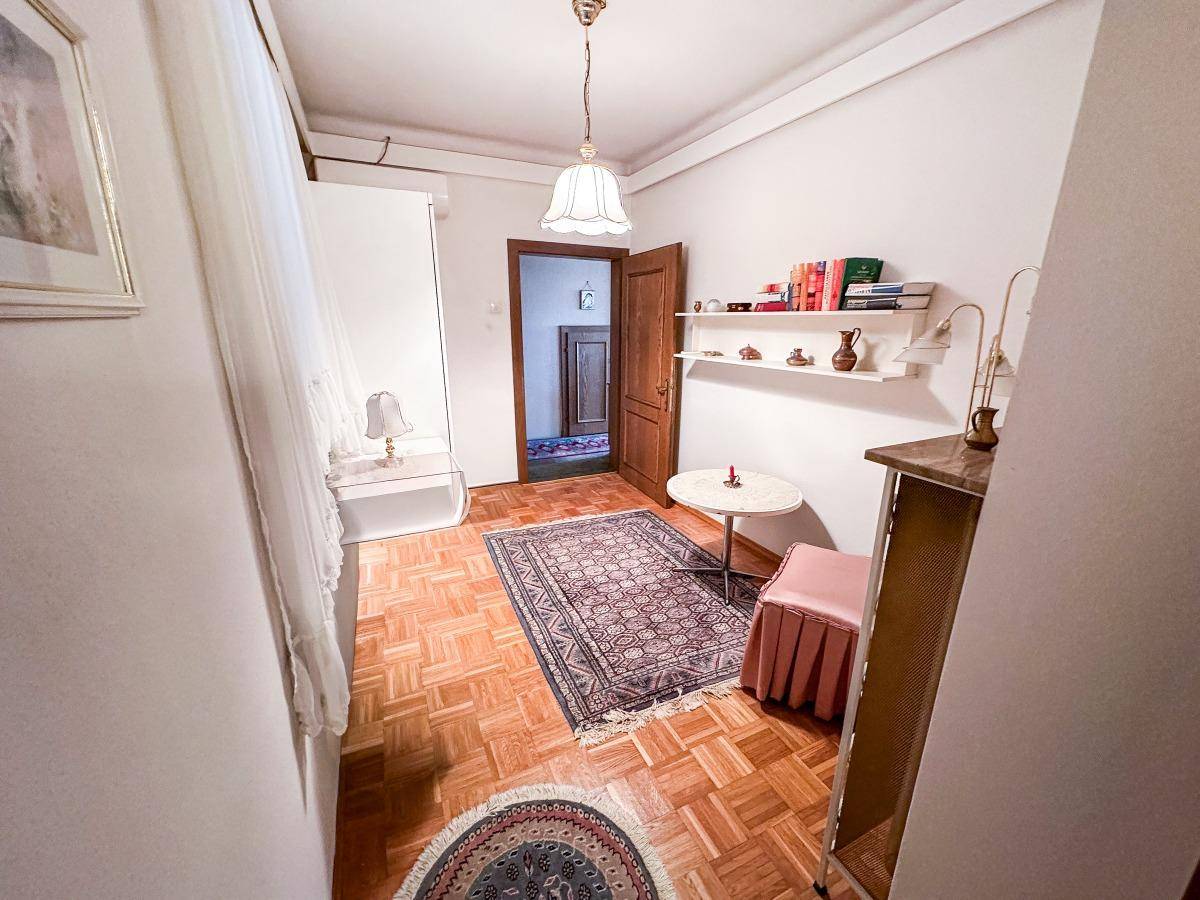 Helles Zimmer mit Parkettboden, Bücherregal und kleinem Tisch.