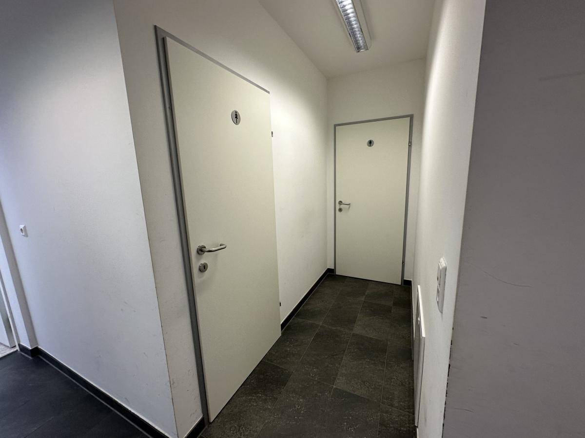 Heller Flur mit zwei weißen Türen, die zu den Sanitäranlagen führen, auf dunklem Fliesenboden.