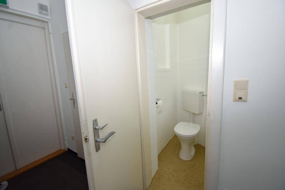 Einfache Toilette mit WC und Waschbecken in einem kleinen, hell gefliesten Raum, praktisch und hell.