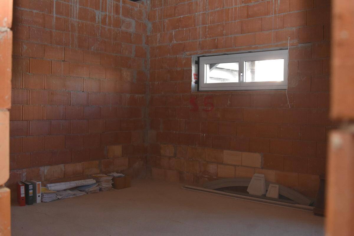 Kleiner Raum im Rohbau mit unverputzten Ziegelwänden und einem kleinen Fenster, das Tageslicht hereinlässt.